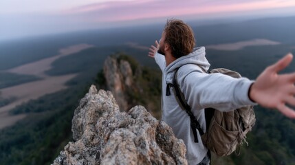 Man on mountaintop, arms outstretched, enjoying the view.  Vast landscape unfolds below, with rugged rocks and valleys visible.  Golden hour light bathes the scene