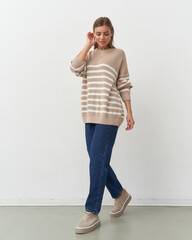 Effortlessly chic woman in striped sweater walks gracefully in a studio setting