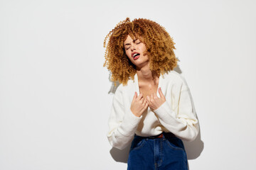 Emotional portrait of a young woman with curly hair, wearing a stylish white sweater and denim...
