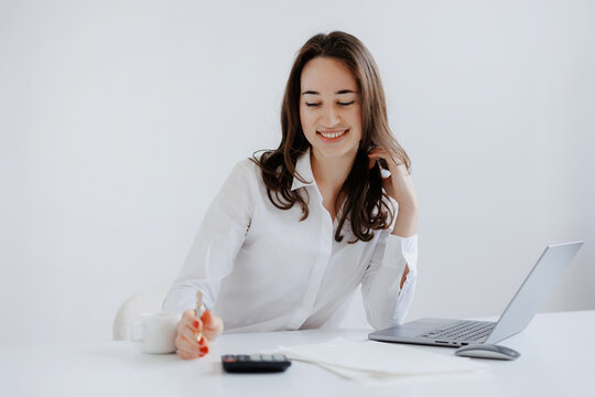 Smiling woman working at a modern desk with a laptop and calculator while organizing documents in a bright office space