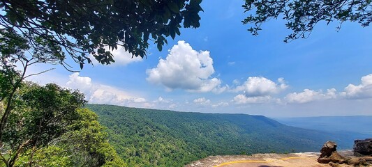 Stunning Panoramic View of Lush Green Mountain Range under a Blue Sky with Puffy Clouds