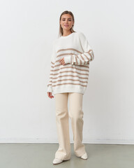 Elegant fashion model poses effortlessly in a chic striped sweater in a studio setting