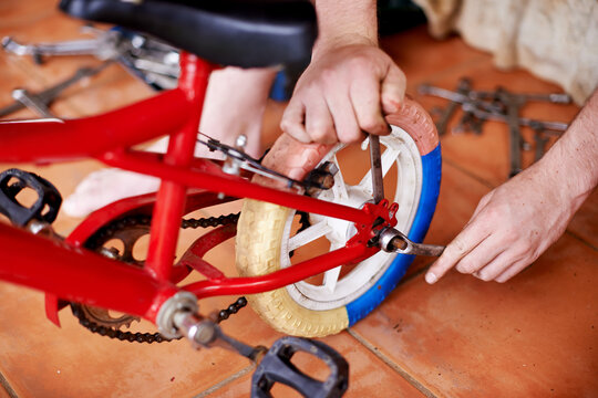 Repair, kids bike and hands of man in workshop for safety, inspection and checking wheel with spanner. Maintenance, service and person fixing bicycle with tools, care and toys for child development