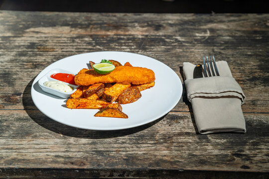 Deep fried fishs and chips, served with remoulade (sauce, mustard, herbs) on white plate. Isolated by wooden table. Food Photography