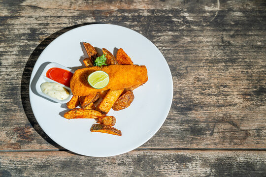 Deep fried fishs and chips, served with remoulade (sauce, mustard, herbs) on white plate. Isolated by wooden table. Food Photography