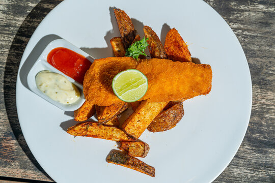 Deep fried fishs and chips, served with remoulade (sauce, mustard, herbs) on white plate. Isolated by wooden table. Food Photography