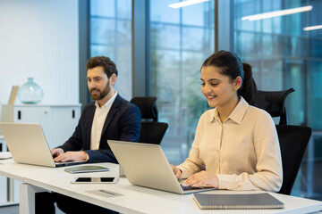 Two colleagues working on laptops in a modern office setting, teamwork concept. The scene shows collaboration and productivity.