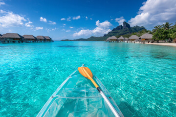 Clear kayak floating on turquoise lagoon near overwater bungalows and tropical island mountain