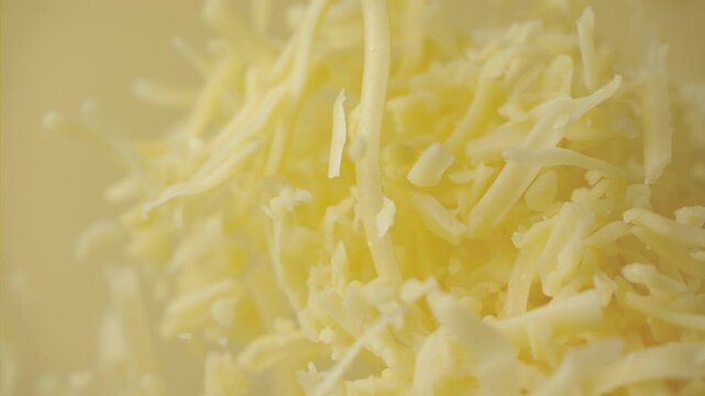 Heap grated cheddar cheese flying in slow motion close up. Shredded yellow parmesan cheese falling in macro. Ungraded raw ProRes footage for grading