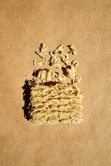 Instant ramen noodle block with scattered broken noodles over brown backdrop
