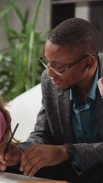 African-American tutor in glasses and schoolboy look peeking at little sister writing letters at home English lesson with native speaker in room slow motion