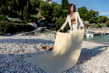 Tourist preparing her beach spot by laying down a striped towel on a picturesque pebble beach,...