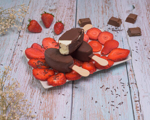 Chocolate ice cream popsicle in a tray with fresh strawberries on a wooden background