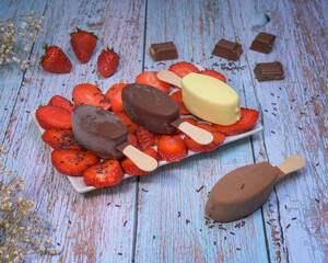 Chocolate ice cream popsicle in a tray with fresh strawberries on a wooden background