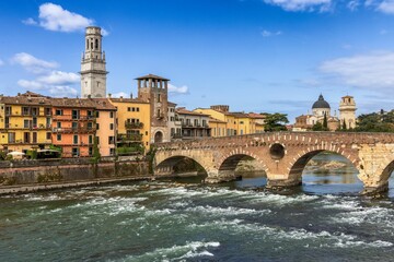 Fototapeta premium Scenic view of Verona's Ponte Pietra and historic buildings under a blue sky.