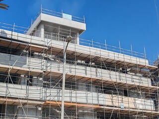 Under construction residential building structure
Highrise Tower Exterior Modern Design Top Level View with blue sky background.
Multi Story Residential Building Site with erected Scaffolding Around
