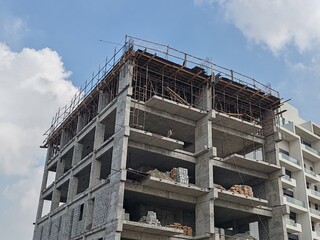 Under construction residential building structure
Highrise Tower Exterior Modern Design Top Level View with blue sky background.
Multi Story Residential Building Site with erected Scaffolding Around