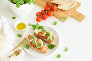 Bruschetta toasts with mozzarella, cherry tomato and basil leaves on white wooden table