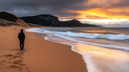 Solitary figure on a sandy beach at sunset, dramatic sky and ocean waves.