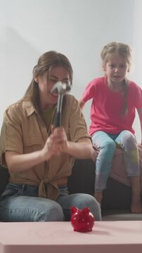 young mother with children breaks piggy bank with hammer with money in form of pig, money box doit