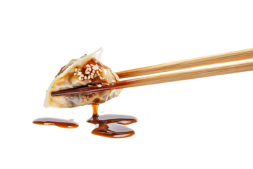 A dumpling held by chopsticks with sesame seeds and sauce dripping down on a black background