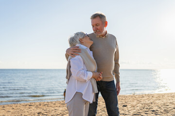 Senior mature couple hugging enjoying outdoor recreation walking on beach. Old husband wife...