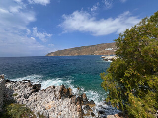 Rocky Coastline with Crystal Clear Aegean Sea and Hillside Village on Amorgos Island, Greece under a Bright Blue Sky