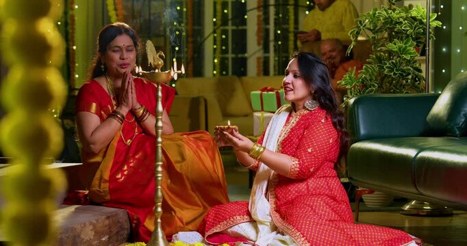 Lighting traditional samai with diya, Indian young girl in ethnic wear and senior mother joyfully celebrating Hindu festival Diwali in evening at home with festive decor and glowing diya illumination