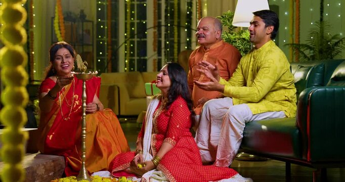 Lighting samai diya indoors during Diwali, Indian family of four including senior mother in saree, father, young girl, and husband smiling together celebrating Hindu festival with joy and tradition