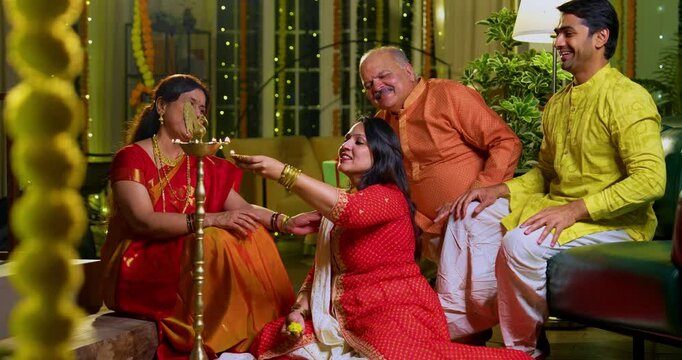 Lighting samai diya indoors during Diwali, Indian family of four including senior mother in saree, father, young girl, and husband smiling together celebrating Hindu festival with joy and tradition