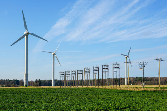 Tall wind turbines with power transmission line generating renewable energy amidst green fields