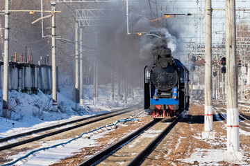 A steam locomotive in clouds of smoke traveling along a railway in winter