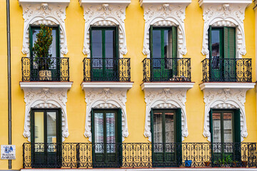 A beautifully detailed yellow building facade with green window shutters in Plaza de San Miguel, Madrid