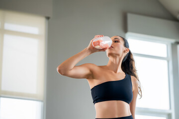 Confident woman in fitness attire drinks a healthy protein smoothie after a workout, embodying...