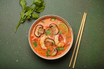 Delicious tom yum soup with shrimps, mushrooms, lime, and coriander served in bowl with chopsticks...
