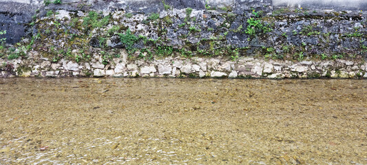 The shallow, clear water of the Gradna River flows gently along a moss-covered stone embankment in Samobor
