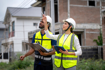 Project manager women and civil engineer wearing safety vests and helmets inspect a housing...
