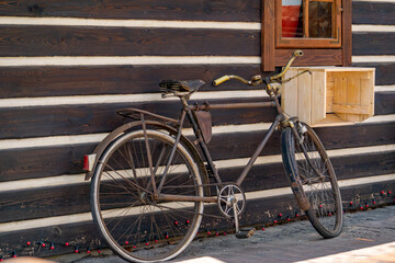 vintage bicycle parked next to a black-and-white timber wall of a traditional countryside house. A wooden crate is mounted under a small window, reflecting soft daylight. The rustic scene evokes a nos