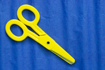 Blue crepe tissue craft paper background with yellow childrens scissors. Craft hobby material concept.