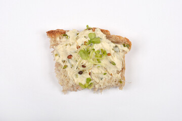 A piece of bread topped with vegan cheese spread and sprouts is isolated on a white surface
