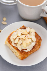 Cinnamon roll topped with cream cheese frosting and sliced almonds served with coffee