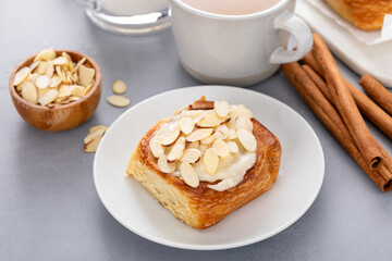 Cinnamon roll topped with cream cheese frosting and sliced almonds served with coffee