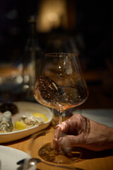 Champagne tasting, Wine glasses are on the table, stylish table setting, A man's hand holds a beautiful elegant glass with rose sparkling wine, an intimate light, a plate with oysters and lemon