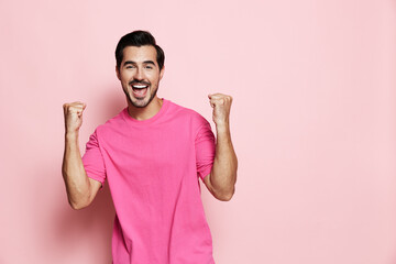 Smiling man wearing bright pink sweater celebrates success with raised fists, exuding joy and...