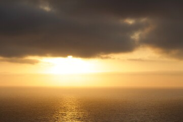 Beautiful ethereal sunset with moody clouds and orange yellow light over calm ocean in San Diego, California