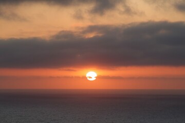 Beautiful pink orange sunset with clouds blocking part of the sun, moody clouds, over ocean in san diego california