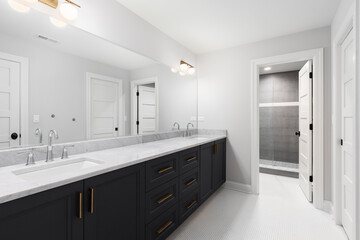 A large bathroom with a dark grey vanity cabinet, white marble countertop, chrome faucetes, white circular tile flooring, and gold hardware.