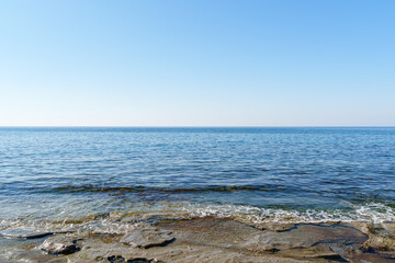 Serene image of a rocky coastline meeting a tranquil sea, with clear blue skies above, ideal for themes of nature, tranquility, and coastal landscapes...