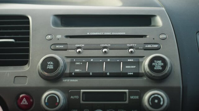 close up of car stereo system showing hand adjusting volume knob as vehicle is powered on, dashboard layout includes control buttons and CD changer with detailed focus on textures and labels