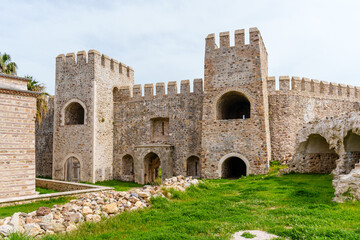 Historic stone castle wall featuring intricate architecture, vintage arched entryways, and a vibrant green lawn with clear skies, ideal for history and architecture enthusiasts...